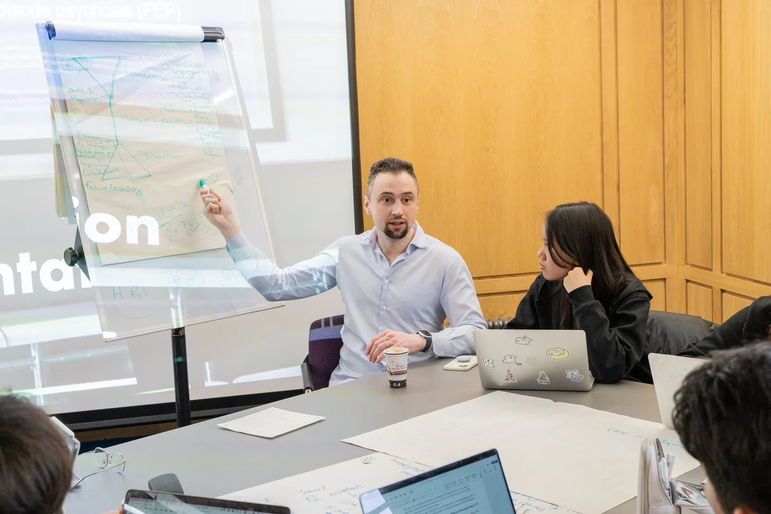 Sam Swidzinski at a flip chart, talking with a group of students around a table